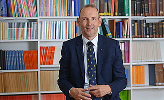 Generalsekretär der EMS, Dr. Dieter Heidtmann, vor einer Bücherwand sitzend.